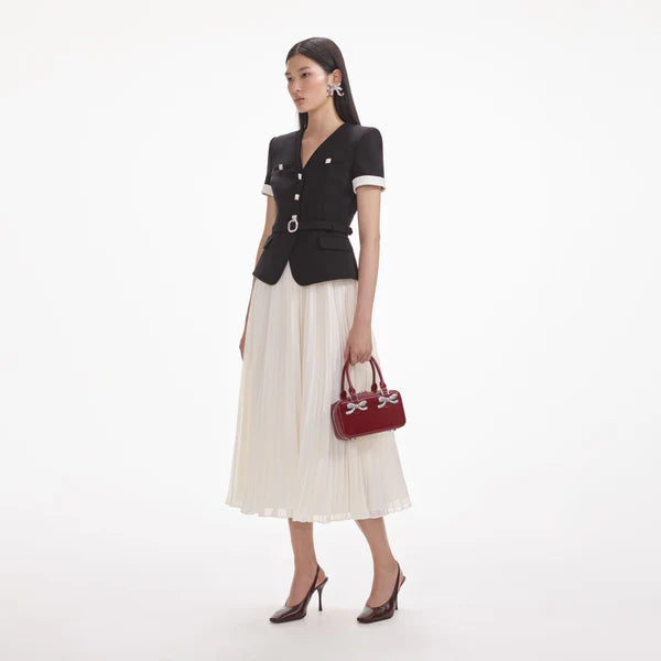 Woman in black top and white skirt holding a red handbag on a white background