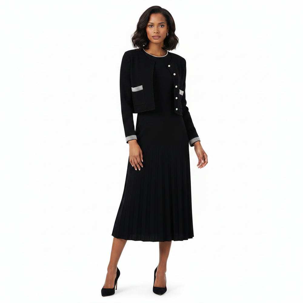 A woman modeling a black long-sleeve midi dress with a pleated skirt, featuring silver button details on the front and silver trim on the cuffs, paired with black high heels against a plain white background.